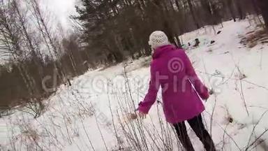 穿着粉红色外套的年轻女子在冬天的森林里散步，触摸树枝